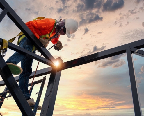 Image of a worker welding together a steel building structure.