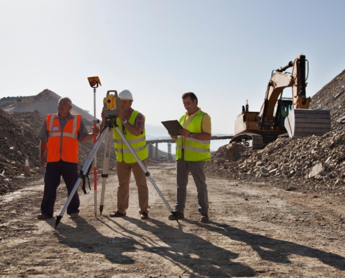 Image of construction workers leveling a site, with an excavator in the background.