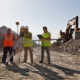 Image of construction workers leveling a site, with an excavator in the background.